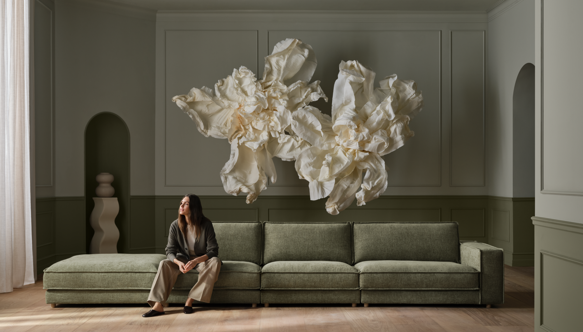 The Viccarbe Savina Sofa in green in a architectural setting with a pendant hanging over and a floor to ceiling window overlooking a vine garden